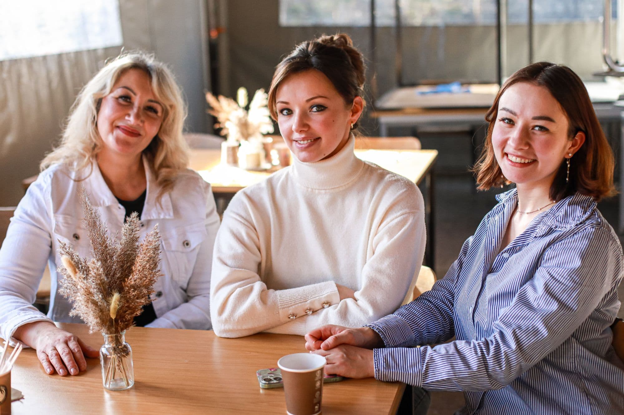 Drei Frauen sitzen lächelnd zusammen an einem Tisch