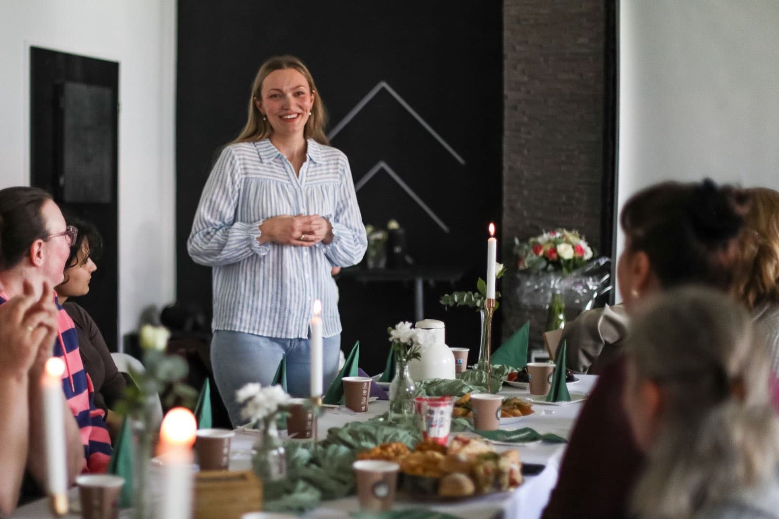 Frau spricht zu einer Gruppe an einem festlich gedeckten Tisch mit Kerzen