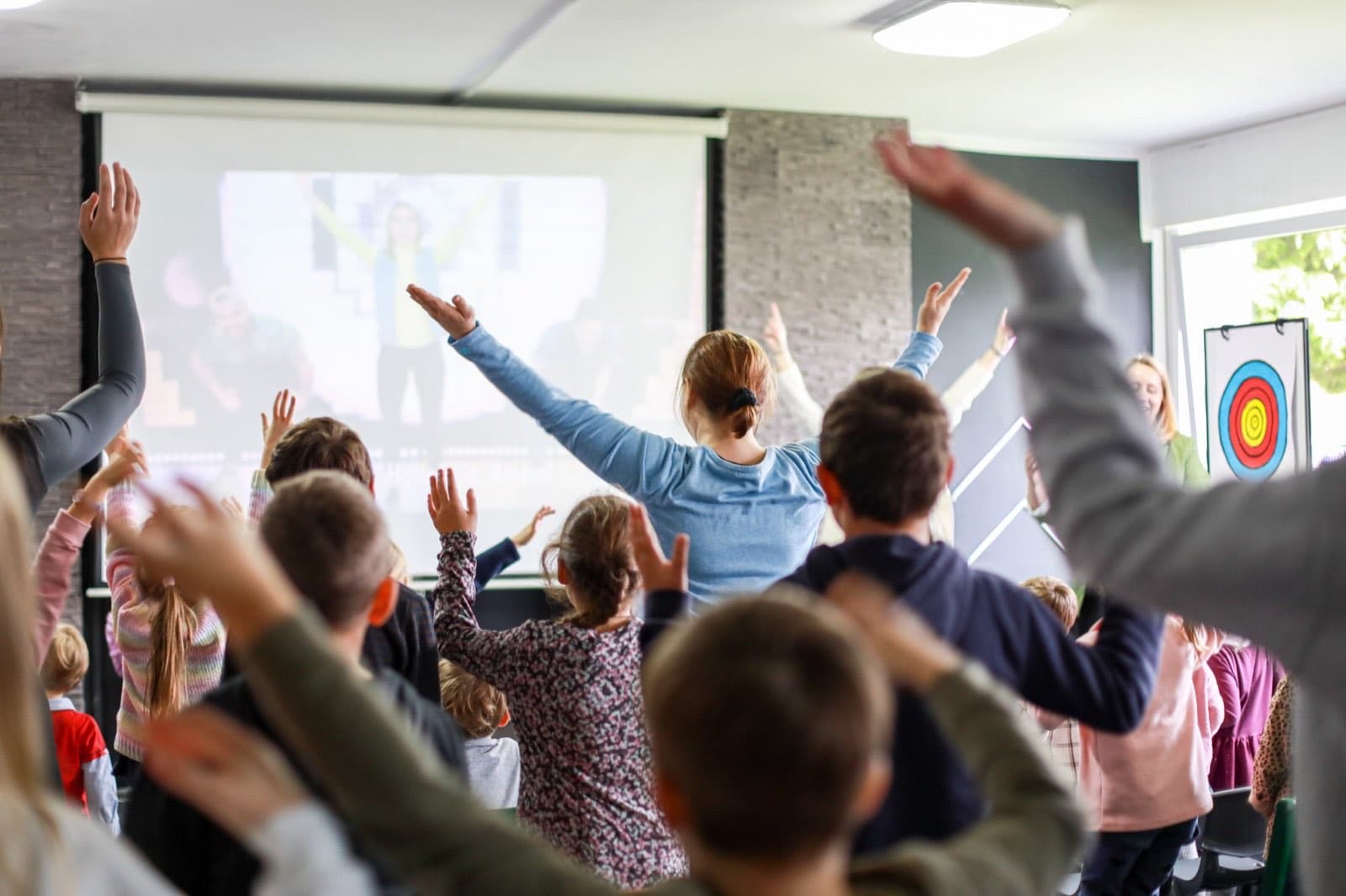 Gruppe von Kindern und Teenagern mit erhobenen Händen vor einer Leinwand